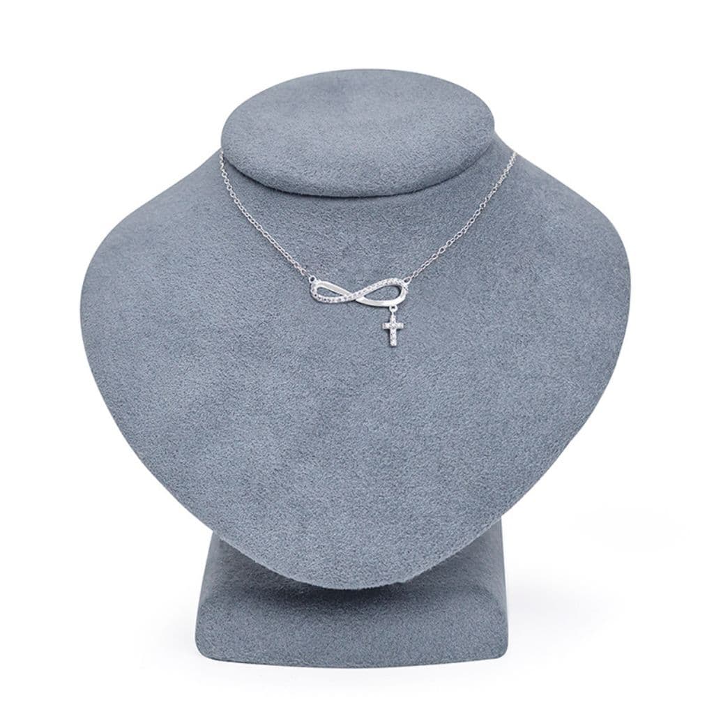 Silver necklace with infinity symbol and cross pendant on a gray jewelry display bust.